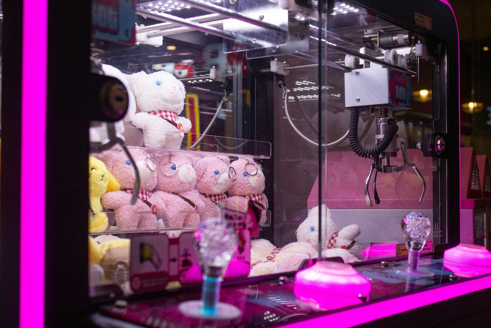 An arcade claw machine, its empty claw hanging above a pile of plush toys