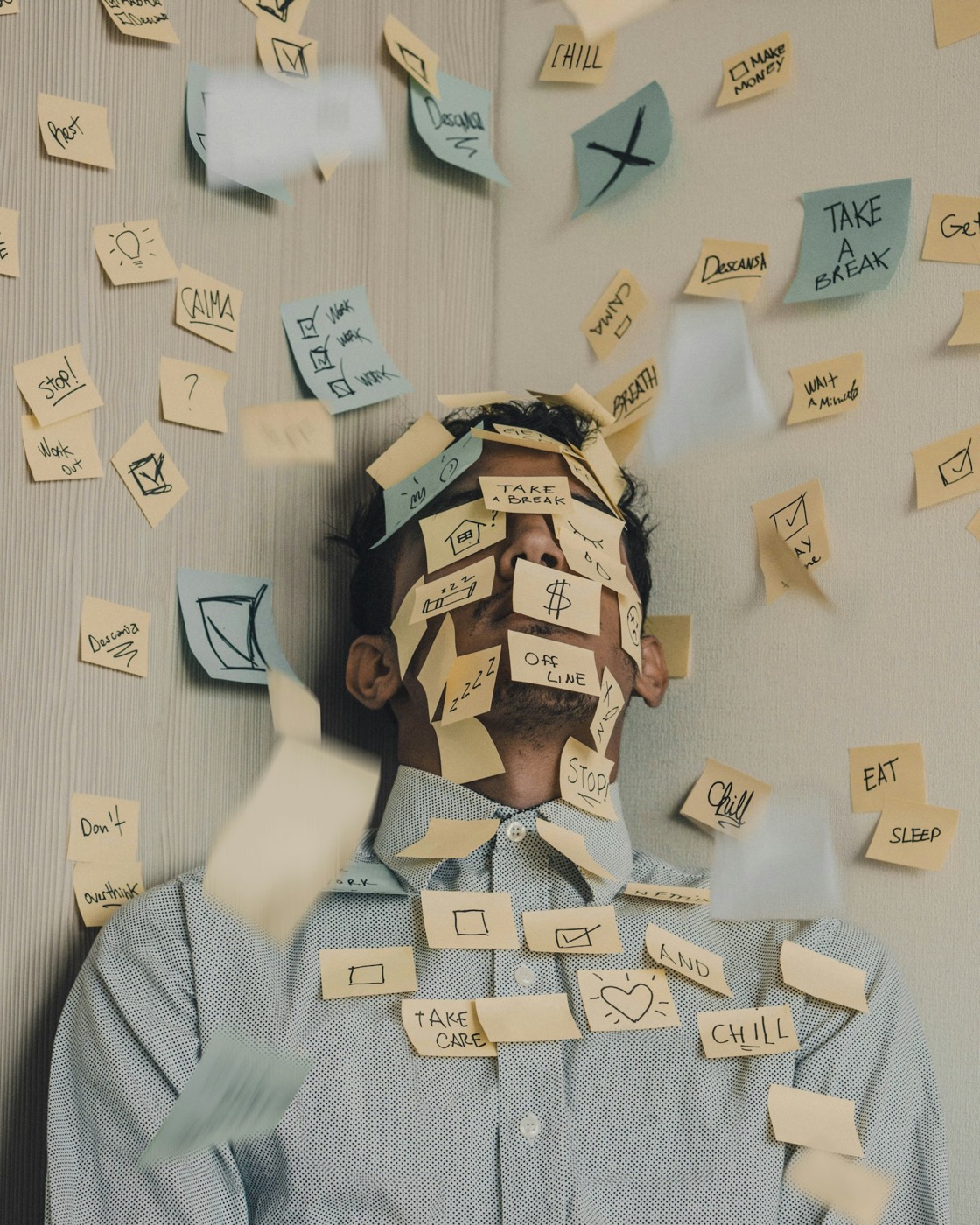 A man buried under sticky notes covering his face and desk